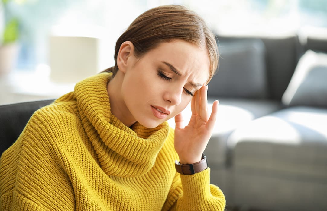 Woman in yellow jumper is experiencing a headache