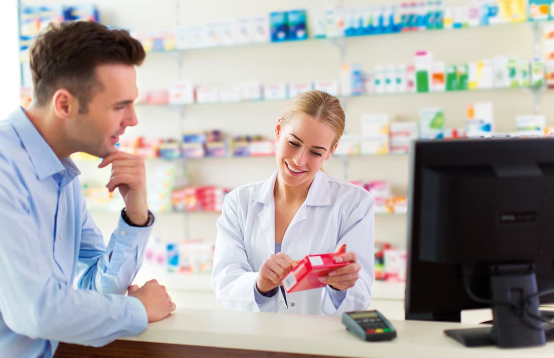 A young man visiting the pharmacy where a pharmacist is showing him one of the products