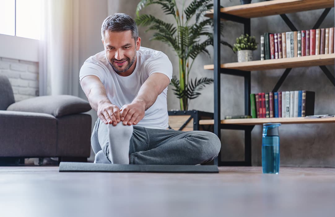 Slightly smiling younger man is stretching on the floor while at home