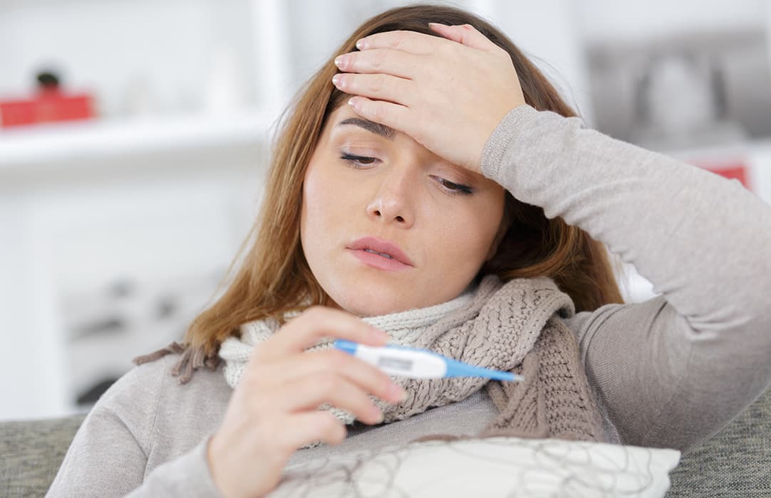 Woman sick in bed with a thermometer in her hand
