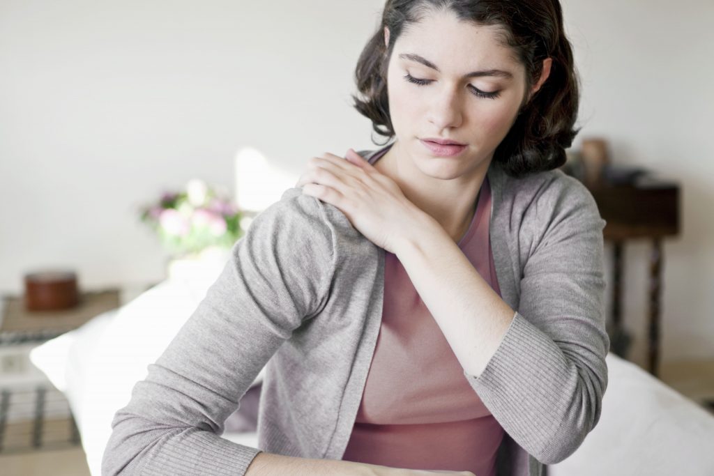 A young woman experiencing shoulder pain while at home