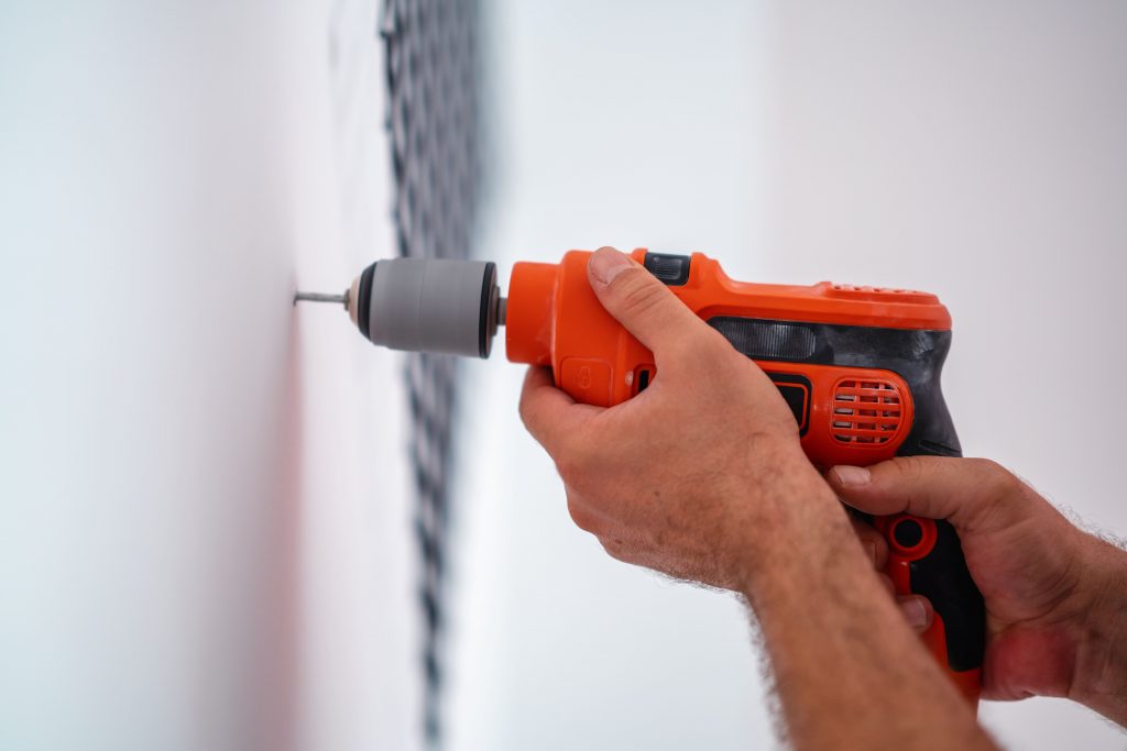 Man holding a power drill against the wall