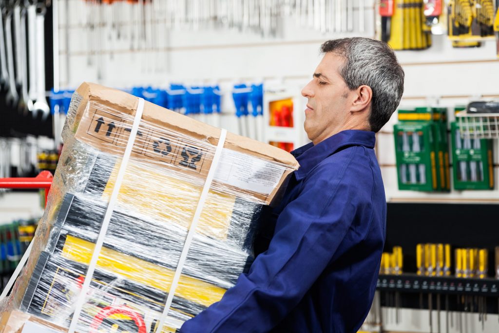 Man in work overalls is carrying a heavy box while in a workshop