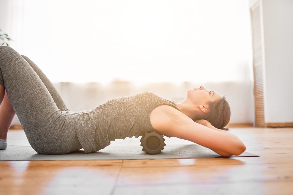 Woman doing yoga lying on massager on rug in gym