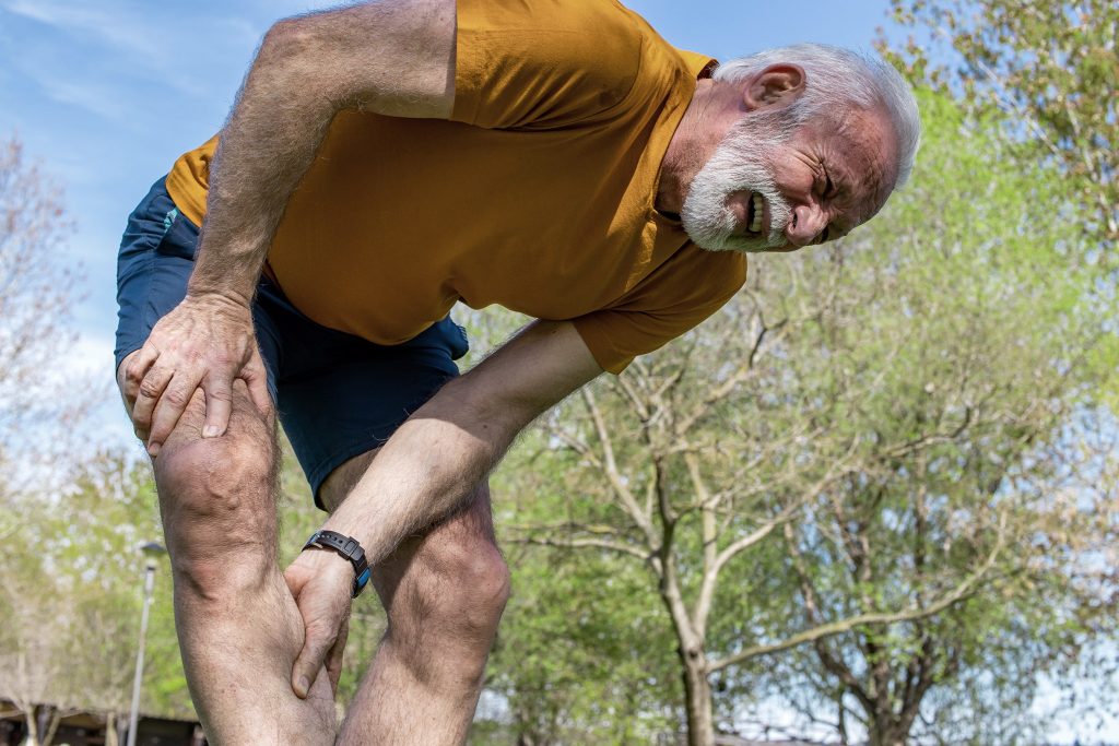 A senior man frowning with muscle pain during training outdoors