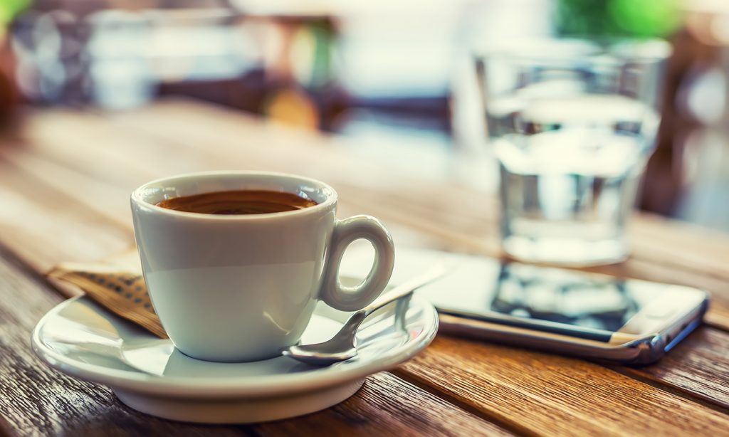 A cup of coffee and a mobile phone on the table with a glass of water in the background