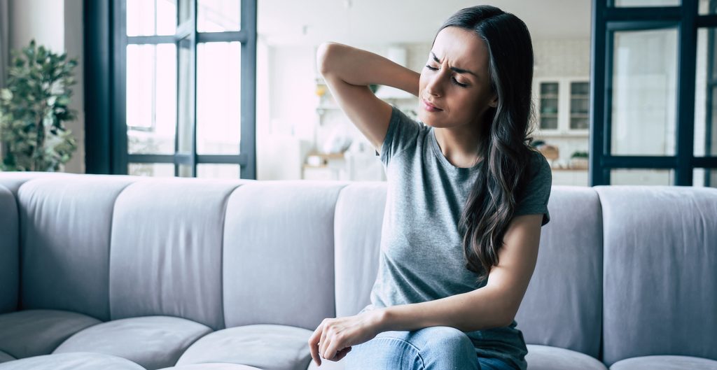 Woman has severe pain in head and neck while sitting on the couch at home