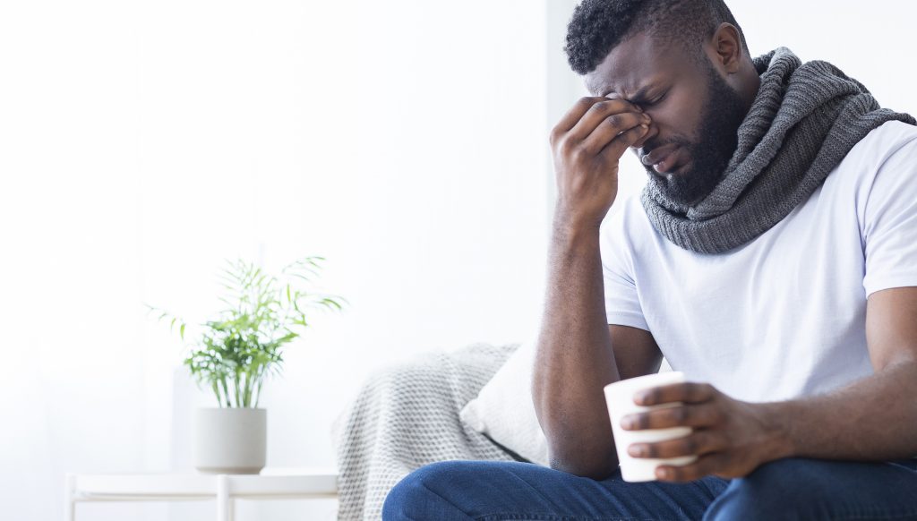 Black man with flu drinking a cup of hot tea at home