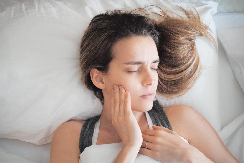 Frustrated young woman touching her cheek and keeping eyes closed while lying in bed at home