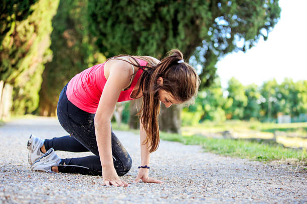 Young woman falling while jogging outdoors on a gravel road